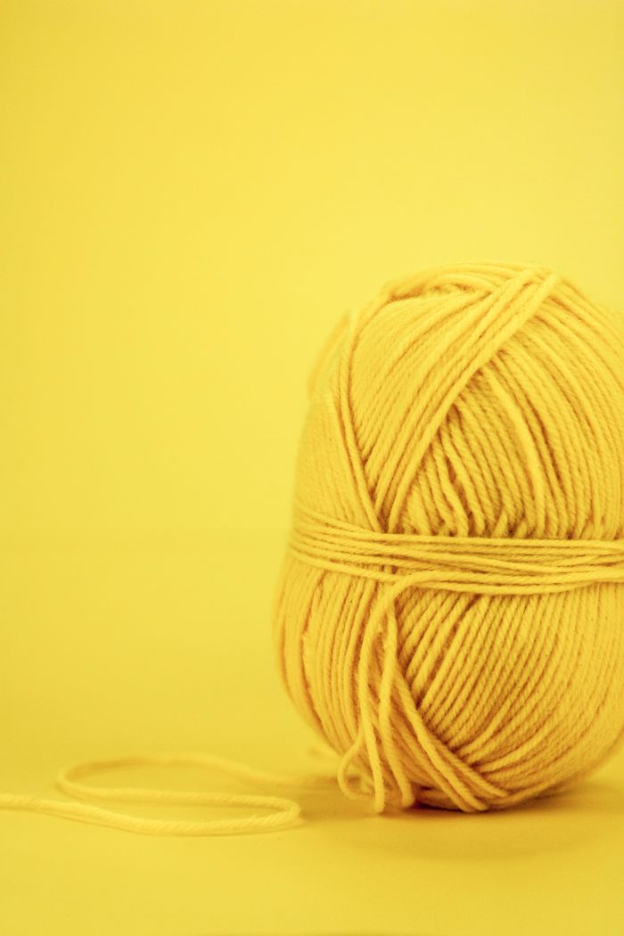 A ball of yellow yarn on a yellow background, perfect for crafting and DIY projects.