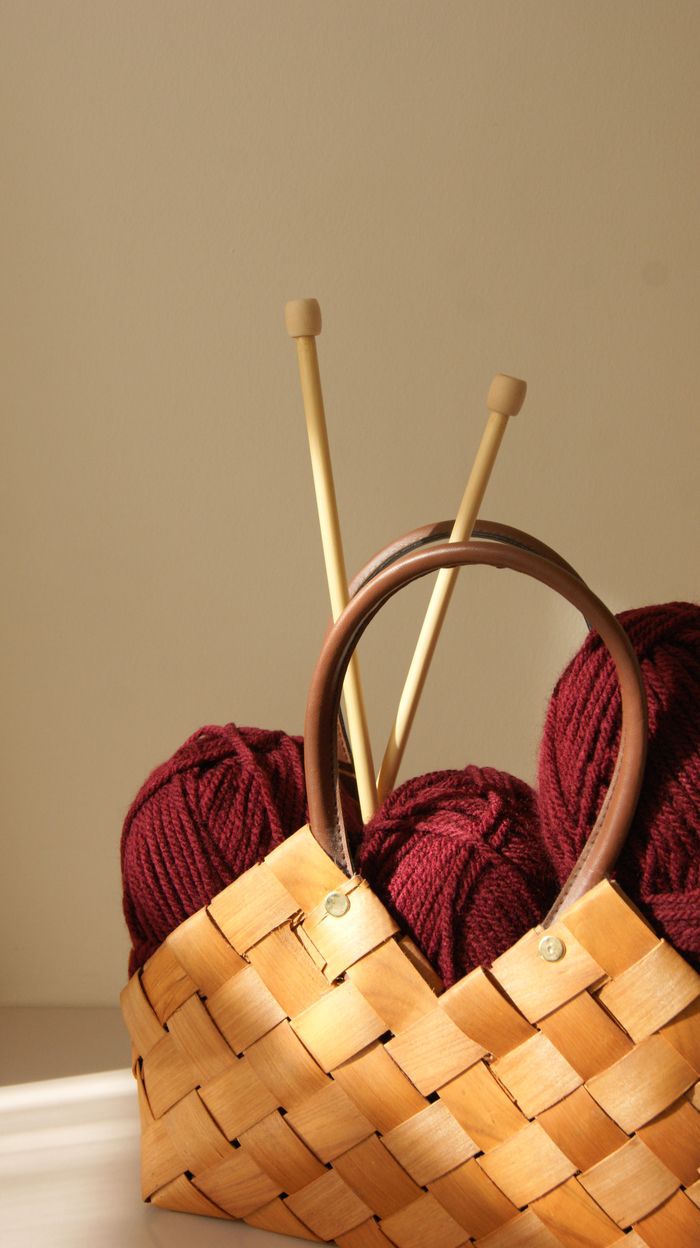 Warm maroon yarn and knitting needles in a wicker basket under soft lighting.
