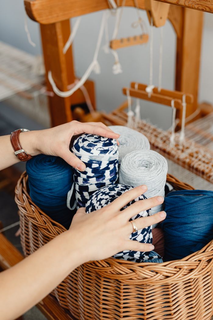 Hands arranging colorful yarn in a basket near a traditional loom setup, ideal for weaving crafts.