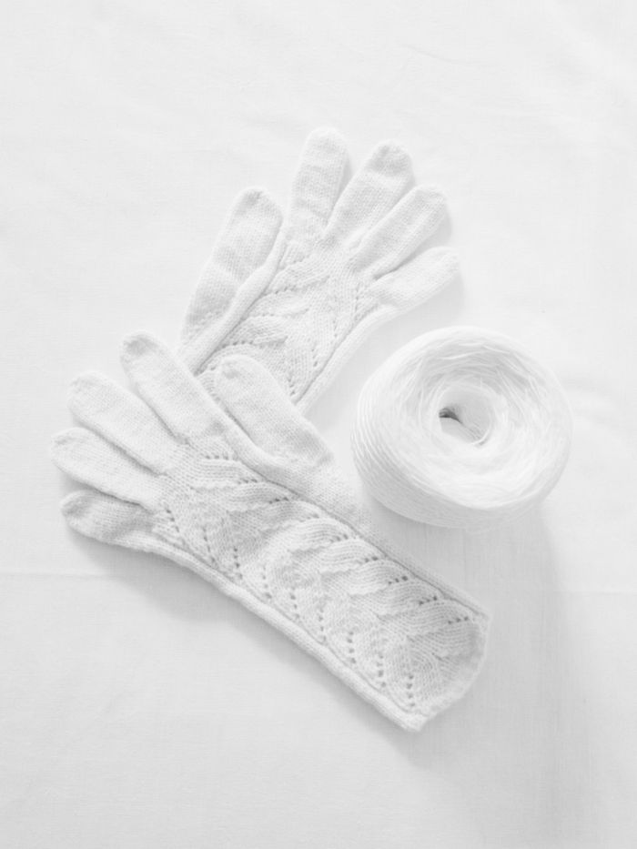 Close-up of white knitted gloves with a matching yarn ball on a white background.